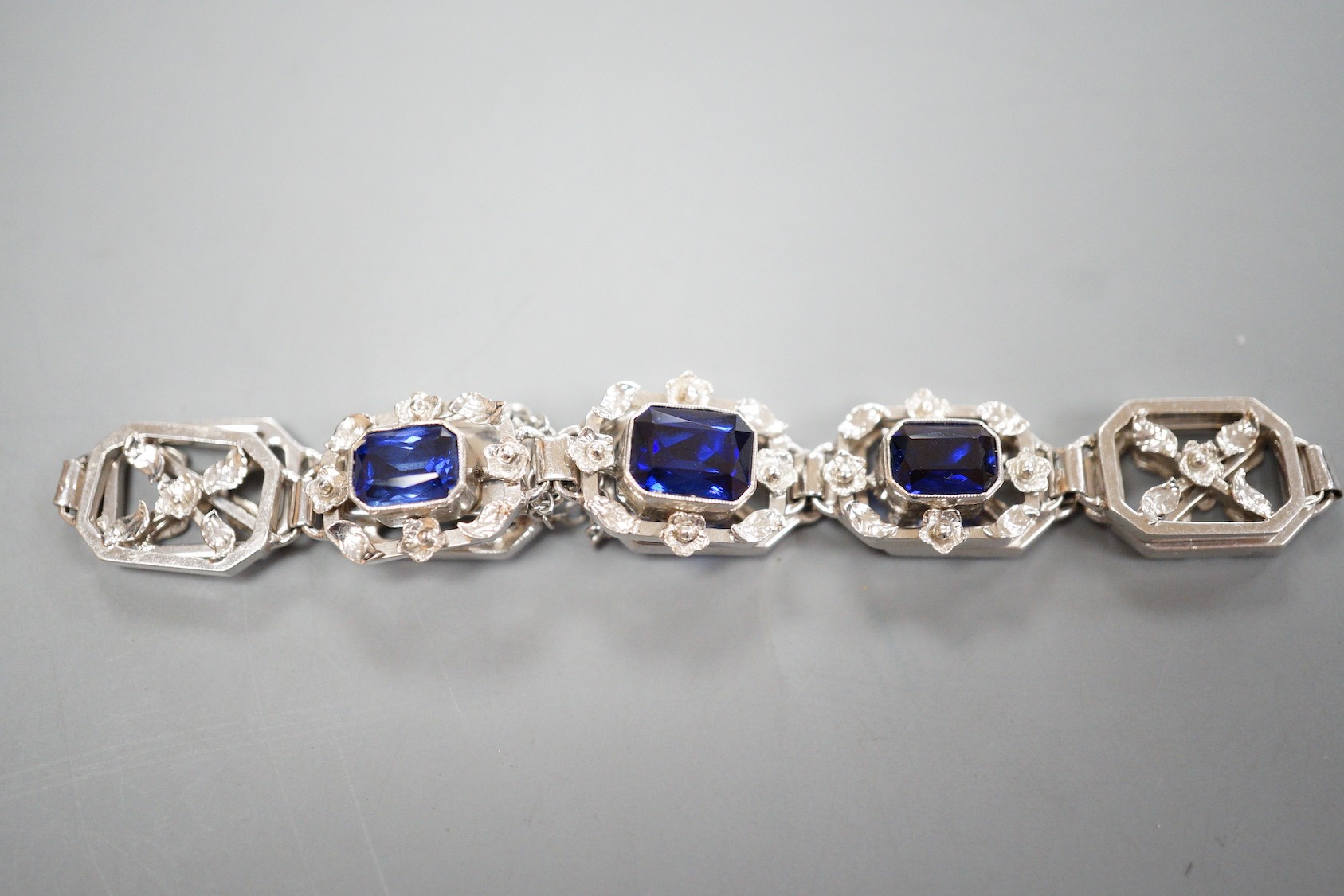 A modern 9ct white metal and three stone emerald cut synthetic sapphire set pierced link bracelet, approx. 18cm, gross weight 16.7 grams.